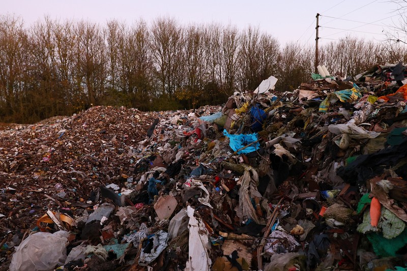 Seorang pria berjalan melewati tumpukan sampah yang dibuang secara ilegal di dataran banjir di sebelah jalan A34, yang memicu penyelidikan Badan Lingkungan Hidup terhadap dugaan kejahatan terorganisir, dekat Kidlington, Oxfordshire, Inggris, 17 November 2025. (REUTERS/Isabel Infantes)