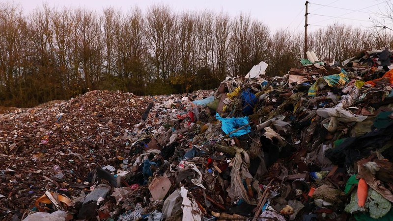 Seorang pria berjalan melewati tumpukan sampah yang dibuang secara ilegal di dataran banjir di sebelah jalan A34, yang memicu penyelidikan Badan Lingkungan Hidup terhadap dugaan kejahatan terorganisir, dekat Kidlington, Oxfordshire, Inggris, 17 November 2025. (REUTERS/Isabel Infantes)