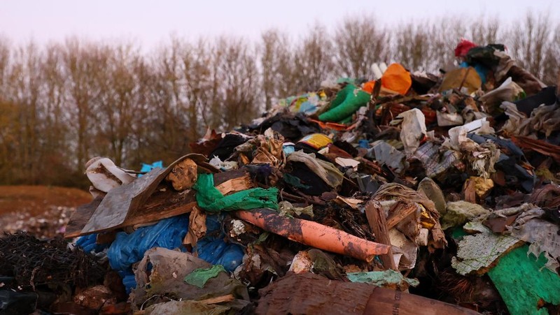 Seorang pria berjalan melewati tumpukan sampah yang dibuang secara ilegal di dataran banjir di sebelah jalan A34, yang memicu penyelidikan Badan Lingkungan Hidup terhadap dugaan kejahatan terorganisir, dekat Kidlington, Oxfordshire, Inggris, 17 November 2025. (REUTERS/Isabel Infantes)