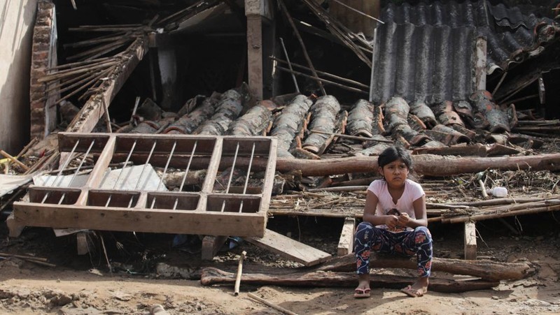 Seorang anak duduk di luar rumah yang rusak akibat tanah longsor setelah enam jam hujan deras yang menghancurkan rumah-rumah dan menyebabkan orang hilang, di Achira, Santa Cruz, Bolivia, 18 November 2025. (REUTERS/Ipa Ibanez)