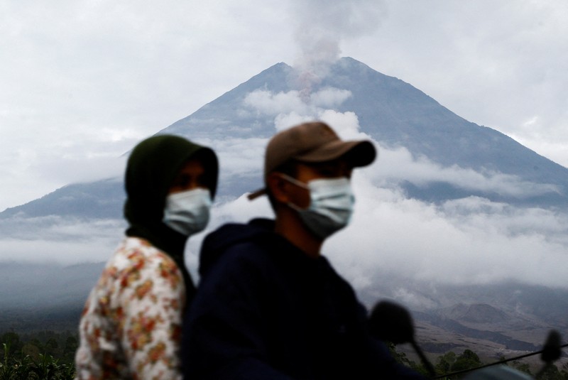 Warga setempat mengendarai sepeda motor saat Gunung Semeru memuntahkan abu vulkanik saat erupsi seperti terlihat di latar belakang, di Desa Supiturang, Lumajang, Provinsi Jawa Timur, Indonesia, 20 November 2025. REUTERS/Dipta Wahyu