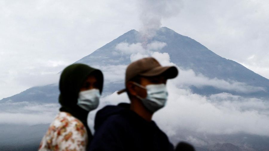 Warga setempat mengendarai sepeda motor saat Gunung Semeru memuntahkan abu vulkanik saat erupsi seperti terlihat di latar belakang, di Desa Supiturang, Lumajang, Provinsi Jawa Timur, Indonesia, 20 November 2025. REUTERS/Dipta Wahyu