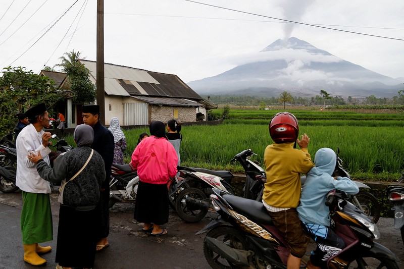 Warga setempat mengendarai sepeda motor saat Gunung Semeru memuntahkan abu vulkanik saat erupsi seperti terlihat di latar belakang, di Desa Supiturang, Lumajang, Provinsi Jawa Timur, Indonesia, 20 November 2025. REUTERS/Dipta Wahyu