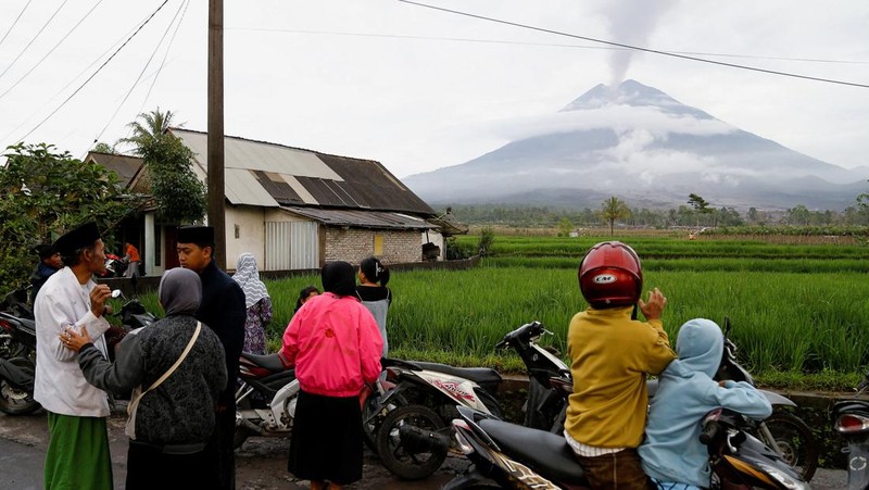 Warga setempat mengendarai sepeda motor saat Gunung Semeru memuntahkan abu vulkanik saat erupsi seperti terlihat di latar belakang, di Desa Supiturang, Lumajang, Provinsi Jawa Timur, Indonesia, 20 November 2025. REUTERS/Dipta Wahyu