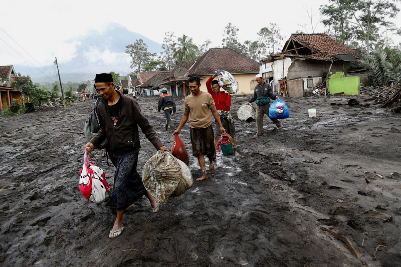 Warga setempat mengendarai sepeda motor saat Gunung Semeru memuntahkan abu vulkanik saat erupsi seperti terlihat di latar belakang, di Desa Supiturang, Lumajang, Provinsi Jawa Timur, Indonesia, 20 November 2025. REUTERS/Dipta Wahyu