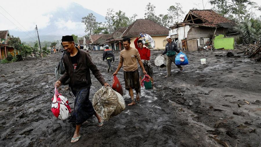 Warga setempat mengendarai sepeda motor saat Gunung Semeru memuntahkan abu vulkanik saat erupsi seperti terlihat di latar belakang, di Desa Supiturang, Lumajang, Provinsi Jawa Timur, Indonesia, 20 November 2025. REUTERS/Dipta Wahyu