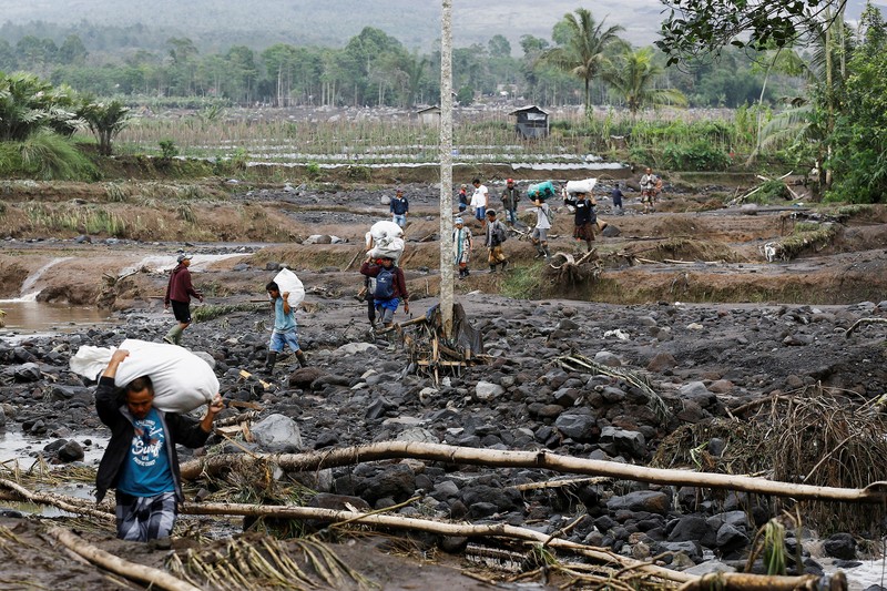 Warga setempat mengendarai sepeda motor saat Gunung Semeru memuntahkan abu vulkanik saat erupsi seperti terlihat di latar belakang, di Desa Supiturang, Lumajang, Provinsi Jawa Timur, Indonesia, 20 November 2025. REUTERS/Dipta Wahyu