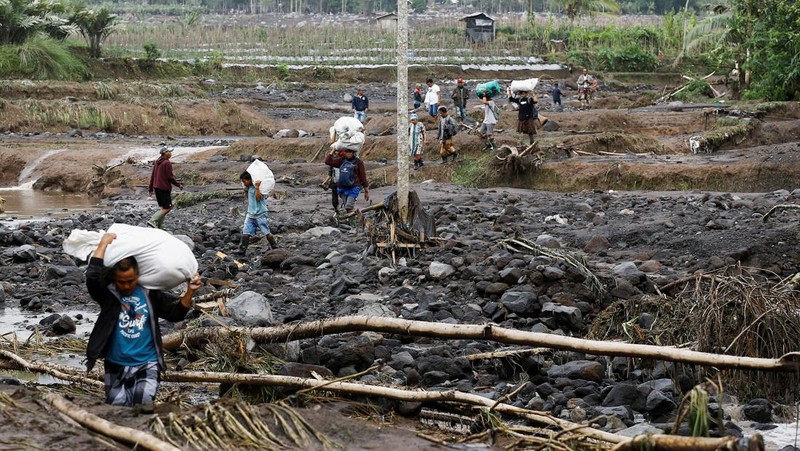 Warga setempat mengendarai sepeda motor saat Gunung Semeru memuntahkan abu vulkanik saat erupsi seperti terlihat di latar belakang, di Desa Supiturang, Lumajang, Provinsi Jawa Timur, Indonesia, 20 November 2025. REUTERS/Dipta Wahyu
