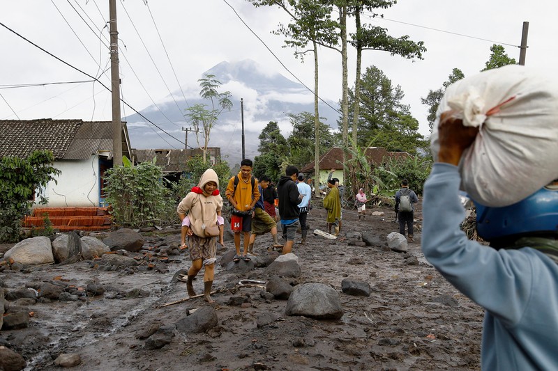 Warga setempat mengendarai sepeda motor saat Gunung Semeru memuntahkan abu vulkanik saat erupsi seperti terlihat di latar belakang, di Desa Supiturang, Lumajang, Provinsi Jawa Timur, Indonesia, 20 November 2025. REUTERS/Dipta Wahyu
