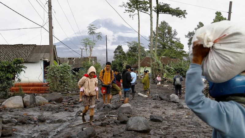 Warga setempat mengendarai sepeda motor saat Gunung Semeru memuntahkan abu vulkanik saat erupsi seperti terlihat di latar belakang, di Desa Supiturang, Lumajang, Provinsi Jawa Timur, Indonesia, 20 November 2025. REUTERS/Dipta Wahyu