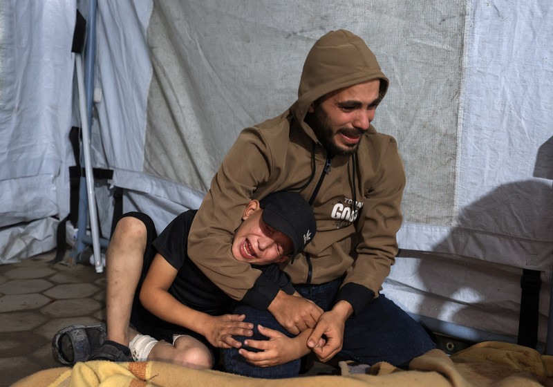 Seorang pria dan seorang anak berduka di dekat jenazah seorang warga Palestina yang tewas dalam serangan udara Israel, menurut petugas medis, di Rumah Sakit Al-Ahli Arab di Kota Gaza, 19 November 2025. REUTERS/Dawoud Abu Alkas