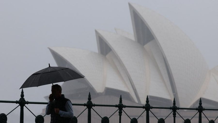 Seorang pria membawa payung berjalan melewati Gedung Opera Sydney di Sydney, Australia, 21 November 2025. REUTERS/Hollie Adams