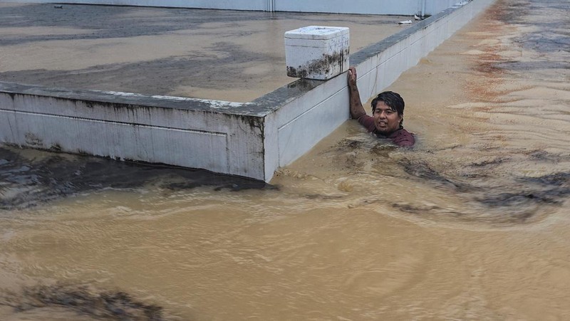 Seorang pria berpegangan pada tiang rambu jalan di jalan yang banjir setelah tersapu ke sana saat pergi keluar untuk mendapatkan persediaan makanan di distrik Hat Yai, yang terdampak hujan lebat yang melanda 10 provinsi di Thailand selatan dan menewaskan beberapa orang, di provinsi Songkhla, Thailand, 24 November 2025. (REUTERS/Sithichai Chootochana)