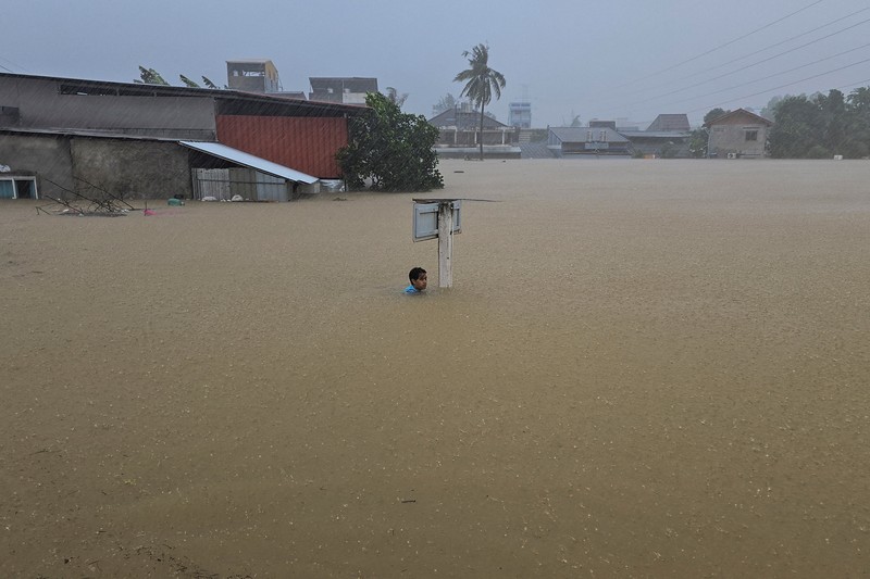 Seorang pria berpegangan pada tiang rambu jalan di jalan yang banjir setelah tersapu ke sana saat pergi keluar untuk mendapatkan persediaan makanan di distrik Hat Yai, yang terdampak hujan lebat yang melanda 10 provinsi di Thailand selatan dan menewaskan beberapa orang, di provinsi Songkhla, Thailand, 24 November 2025. (REUTERS/Sithichai Chootochana)