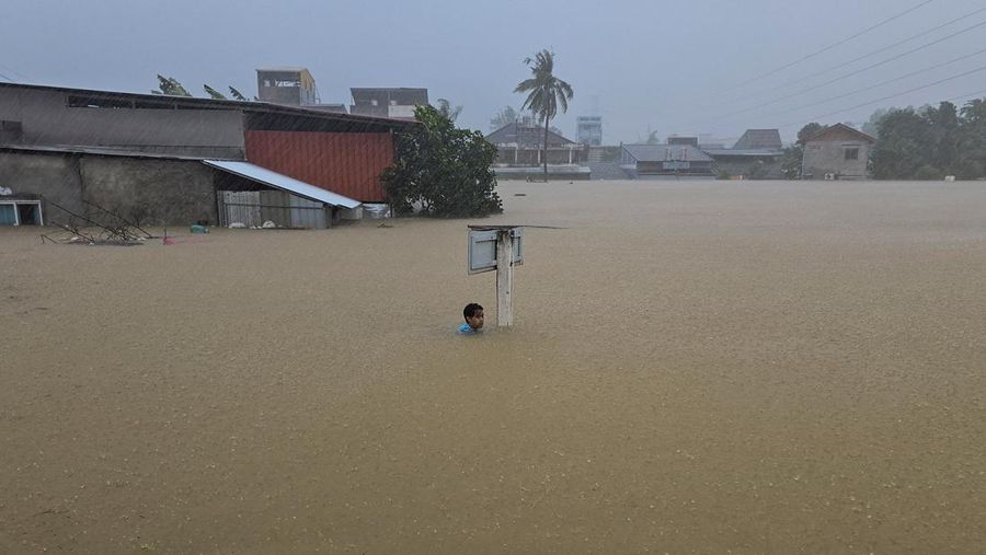 Seorang pria berpegangan pada tiang rambu jalan di jalan yang banjir setelah tersapu ke sana saat pergi keluar untuk mendapatkan persediaan makanan di distrik Hat Yai, yang terdampak hujan lebat yang melanda 10 provinsi di Thailand selatan dan menewaskan beberapa orang, di provinsi Songkhla, Thailand, 24 November 2025. (REUTERS/Sithichai Chootochana)