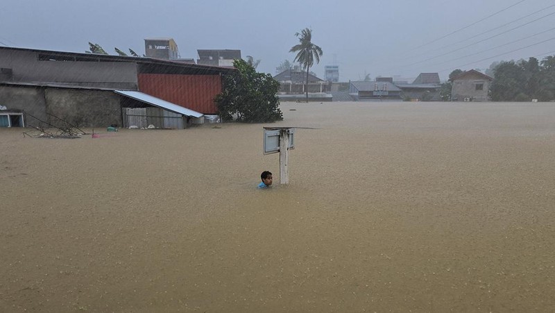 Seorang pria berpegangan pada tiang rambu jalan di jalan yang banjir setelah tersapu ke sana saat pergi keluar untuk mendapatkan persediaan makanan di distrik Hat Yai, yang terdampak hujan lebat yang melanda 10 provinsi di Thailand selatan dan menewaskan beberapa orang, di provinsi Songkhla, Thailand, 24 November 2025. (REUTERS/Sithichai Chootochana)