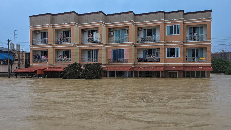 Seorang pria berpegangan pada tiang rambu jalan di jalan yang banjir setelah tersapu ke sana saat pergi keluar untuk mendapatkan persediaan makanan di distrik Hat Yai, yang terdampak hujan lebat yang melanda 10 provinsi di Thailand selatan dan menewaskan beberapa orang, di provinsi Songkhla, Thailand, 24 November 2025. (REUTERS/Sithichai Chootochana)