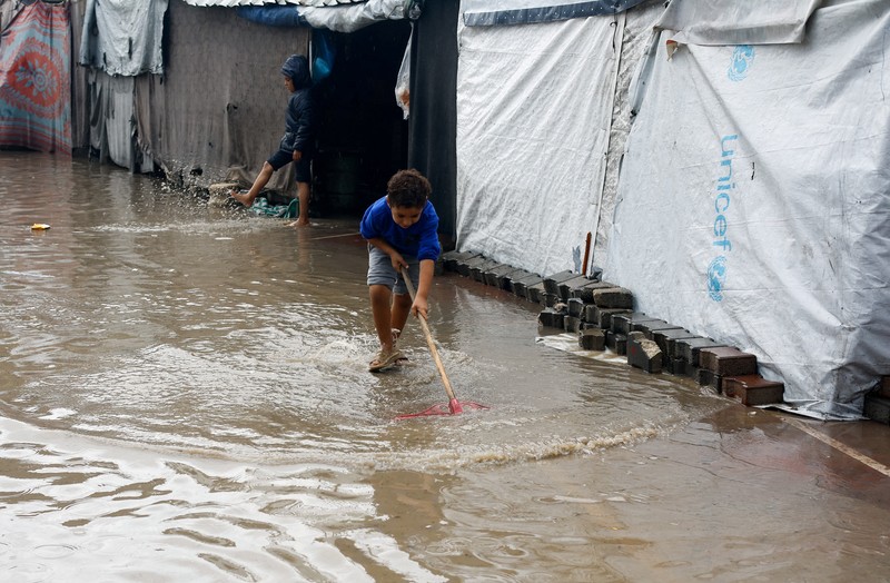 Warga Palestina yang mengungsi berkumpul di samping tenda-tenda di daerah yang banjir, pada hari hujan di Kota Gaza, 25 November 2025. (REUTERS/Mahmoud Issa)