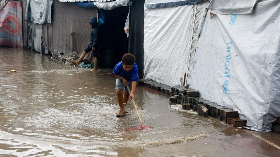 Warga Palestina yang mengungsi berkumpul di samping tenda-tenda di daerah yang banjir, pada hari hujan di Kota Gaza, 25 November 2025. (REUTERS/Mahmoud Issa)