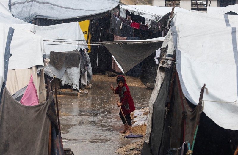 Warga Palestina yang mengungsi berkumpul di samping tenda-tenda di daerah yang banjir, pada hari hujan di Kota Gaza, 25 November 2025. (REUTERS/Mahmoud Issa)
