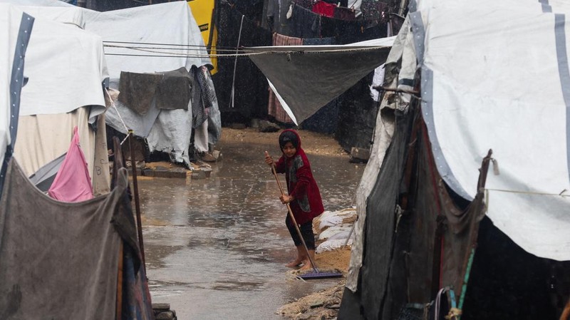 Warga Palestina yang mengungsi berkumpul di samping tenda-tenda di daerah yang banjir, pada hari hujan di Kota Gaza, 25 November 2025. (REUTERS/Mahmoud Issa)