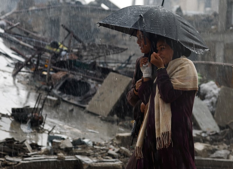 Warga Palestina yang mengungsi berkumpul di samping tenda-tenda di daerah yang banjir, pada hari hujan di Kota Gaza, 25 November 2025. (REUTERS/Mahmoud Issa)