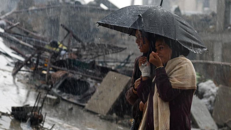 Warga Palestina yang mengungsi berkumpul di samping tenda-tenda di daerah yang banjir, pada hari hujan di Kota Gaza, 25 November 2025. (REUTERS/Mahmoud Issa)