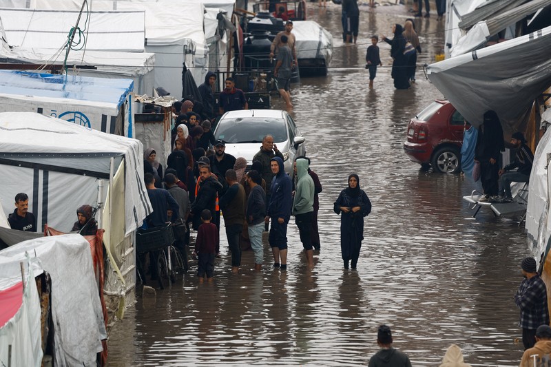 Warga Palestina yang mengungsi berkumpul di samping tenda-tenda di daerah yang banjir, pada hari hujan di Kota Gaza, 25 November 2025. (REUTERS/Mahmoud Issa)