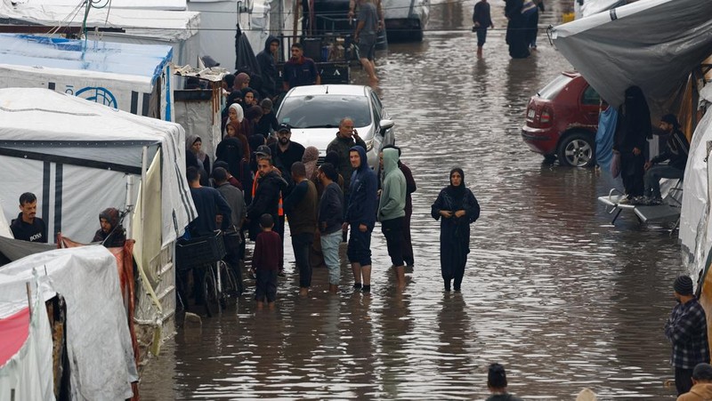 Warga Palestina yang mengungsi berkumpul di samping tenda-tenda di daerah yang banjir, pada hari hujan di Kota Gaza, 25 November 2025. (REUTERS/Mahmoud Issa)