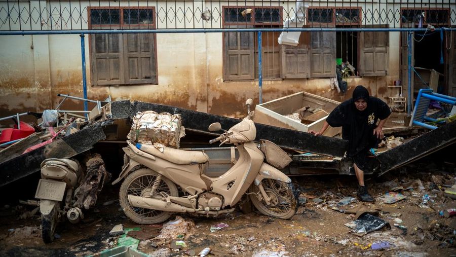 Seorang wanita berjalan di samping sepeda motor yang rusak di daerah banjir di distrik Hat Yai, provinsi Songkhla, Thailand, 28 November 2025. (REUTERS/Athit Perawongmetha)