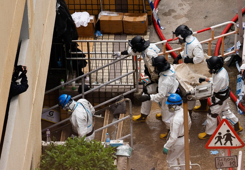 Petugas polisi membawa jenazah korban yang ditemukan dari blok perumahan yang rusak akibat kebakaran di kompleks perumahan Wang Fuk Court setelah kebakaran mematikan, di Tai Po, Hong Kong, Tiongkok, 1 Desember 2025. (REUTERS/Maxim Shemetov)