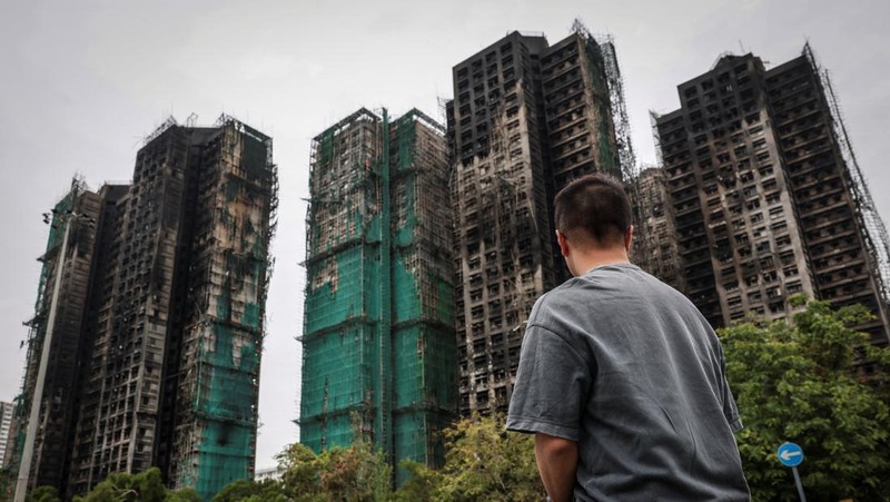 Seorang penghuni Wang Chi House, satu-satunya bangunan yang tidak terkena dampak langsung kebakaran mematikan di kompleks perumahan Wang Fuk Court, menggulingkan kopernya melintasi jalan setelah mengambil barang-barang miliknya, di Tai Po, Hong Kong, Tiongkok, 3 Desember 2025. (REUTERS/Maxim Shemetov)