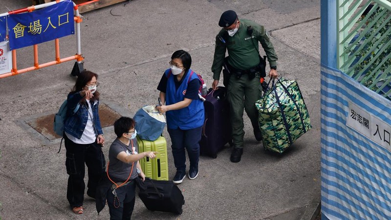 Seorang penghuni Wang Chi House, satu-satunya bangunan yang tidak terkena dampak langsung kebakaran mematikan di kompleks perumahan Wang Fuk Court, menggulingkan kopernya melintasi jalan setelah mengambil barang-barang miliknya, di Tai Po, Hong Kong, Tiongkok, 3 Desember 2025. (REUTERS/Maxim Shemetov)