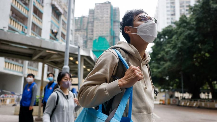 Seorang penghuni Wang Chi House, satu-satunya bangunan yang tidak terkena dampak langsung kebakaran mematikan di kompleks perumahan Wang Fuk Court, menggulingkan kopernya melintasi jalan setelah mengambil barang-barang miliknya, di Tai Po, Hong Kong, Tiongkok, 3 Desember 2025. (REUTERS/Maxim Shemetov)