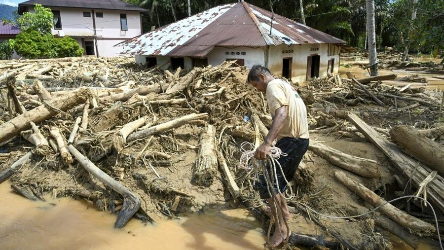 Warga desa menebang kayu-kayu yang hanyut oleh banjir bandang, berniat menggunakannya sebagai material untuk membangun kembali rumah mereka yang rusak di Garoga, Provinsi Sumatera Utara, Kamis (4/12/2025). (YT HARIONO / AFP)