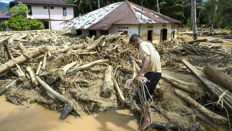 Warga desa menebang kayu-kayu yang hanyut oleh banjir bandang, berniat menggunakannya sebagai material untuk membangun kembali rumah mereka yang rusak di Garoga, Provinsi Sumatera Utara, Kamis (4/12/2025). (YT HARIONO / AFP)