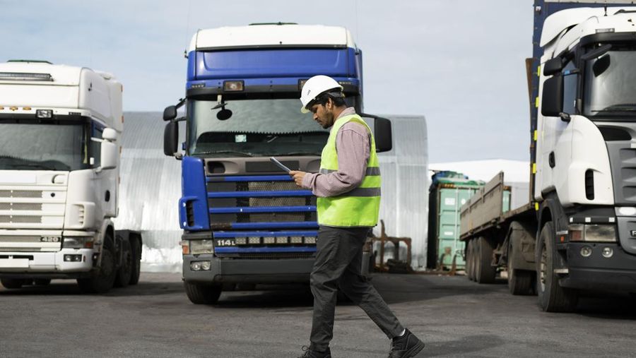 Ilustrasi seorang pekerja berjalan melewati parkiran truk. (Dok. Freepik)