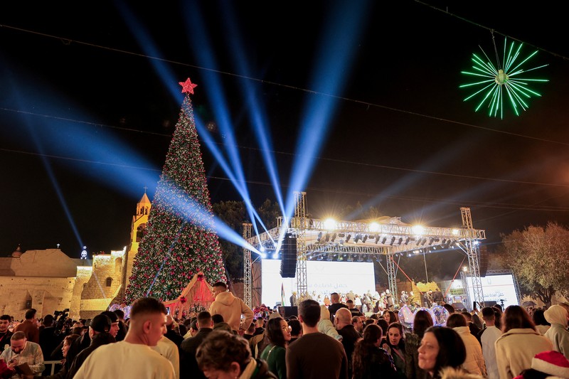 Warga Palestina melihat pohon Natal di Lapangan Manger di luar Gereja Kelahiran Yesus, Betlehem, Tepi Barat, Sabtu (6/12/2025). (REUTERS/Mussa Qawasma)