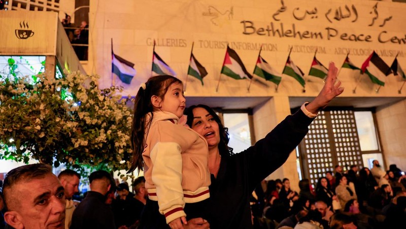 Warga Palestina melihat pohon Natal di Lapangan Manger di luar Gereja Kelahiran Yesus, Betlehem, Tepi Barat, Sabtu (6/12/2025). (REUTERS/Mussa Qawasma)
