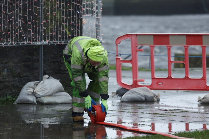 A worker holds a hose as he prepares a flood barrier defence system at the Spanish Arch, as storm named Bram approaches, in Galway, Ireland, December 9, 2025. REUTERS/Clodagh Kilcoyne