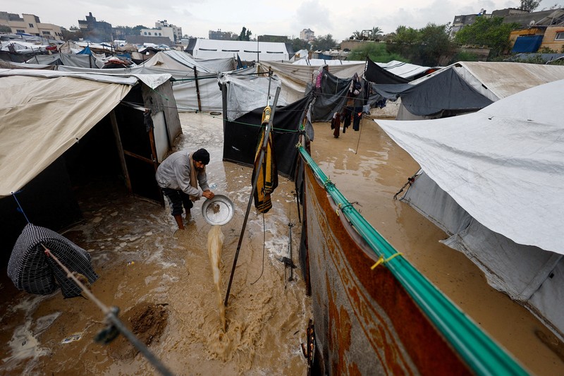 Seorang pria Palestina pengungsi membersihkan air berlumpur di kamp tenda yang tergenang banjir pada hari hujan di Nuseirat, Jalur Gaza tengah, 12 Desember 2025. (REUTERS/Mahmoud Issa)