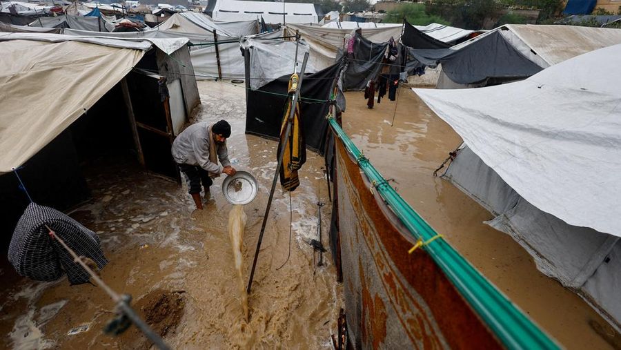 Seorang pria Palestina pengungsi membersihkan air berlumpur di kamp tenda yang tergenang banjir pada hari hujan di Nuseirat, Jalur Gaza tengah, 12 Desember 2025. (REUTERS/Mahmoud Issa)