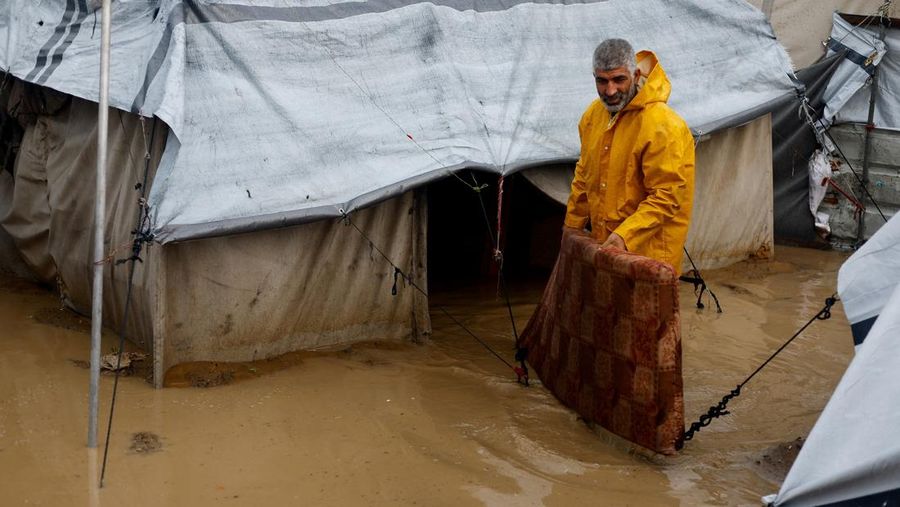 Seorang pria Palestina pengungsi membersihkan air berlumpur di kamp tenda yang tergenang banjir pada hari hujan di Nuseirat, Jalur Gaza tengah, 12 Desember 2025. (REUTERS/Mahmoud Issa)
