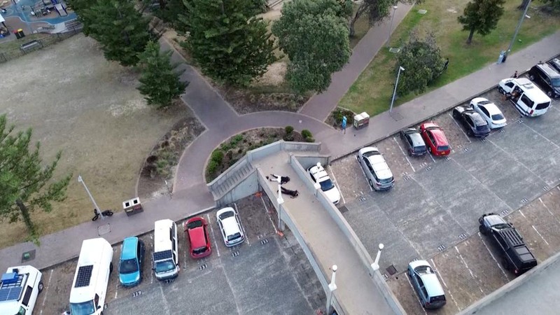 Sebuah tayangan drone menunjukkan salah satu tersangka pelaku penembakan di jembatan penyeberangan, di samping tersangka pelaku penembakan lainnya yang sedang berbaring, sementara para korban tergeletak di tanah, setelah insiden penembakan di Pantai Bondi, Sydney, Australia, 14 Desember 2025, dalam cuplikan layar yang diperoleh dari video media sosial. (@bonusik28 via X/via REUTERS)