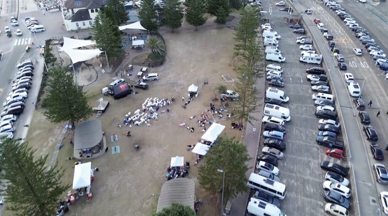 Sebuah tayangan drone menunjukkan salah satu tersangka pelaku penembakan di jembatan penyeberangan, di samping tersangka pelaku penembakan lainnya yang sedang berbaring, sementara para korban tergeletak di tanah, setelah insiden penembakan di Pantai Bondi, Sydney, Australia, 14 Desember 2025, dalam cuplikan layar yang diperoleh dari video media sosial. (@bonusik28 via X/via REUTERS)