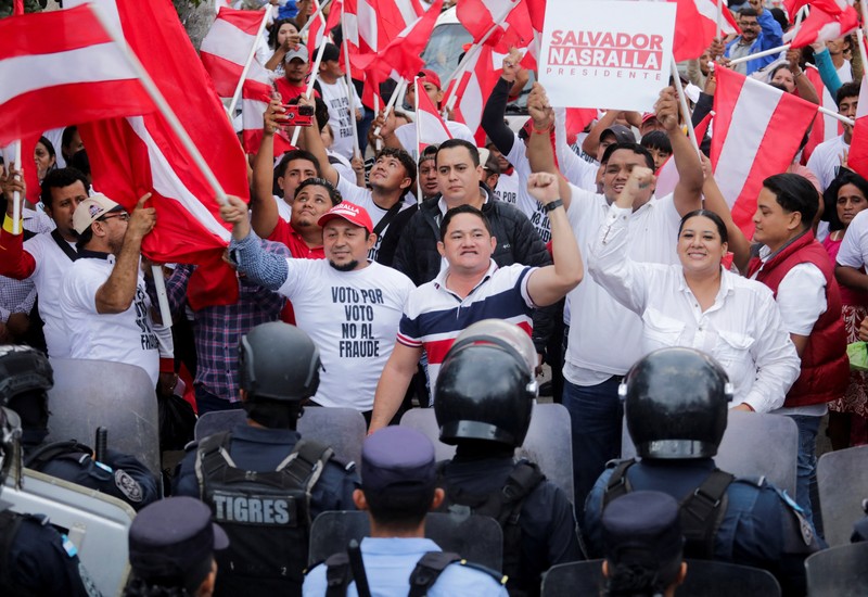 Para pendukung calon presiden Salvador Nasralla dari Partai Liberal berunjuk rasa di depan polisi anti huru hara, lebih dari dua minggu setelah pemilihan presiden, karena penghitungan suara masih terhenti di tengah surat suara yang belum dihitung, tuduhan kecurangan, dan kegagalan sistem pemilu, di Tegucigalpa, Honduras, 15 Desember 2025. (REUTERS/Fredy Rodriguez)