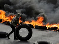 Seorang pendukung pemerintah menggulirkan ban di samping penghalang jalan yang terbakar hampir dua minggu setelah pemilihan presiden, sementara penghitungan suara masih terhenti di tengah surat suara yang belum dihitung, tuduhan kecurangan, dan kegag