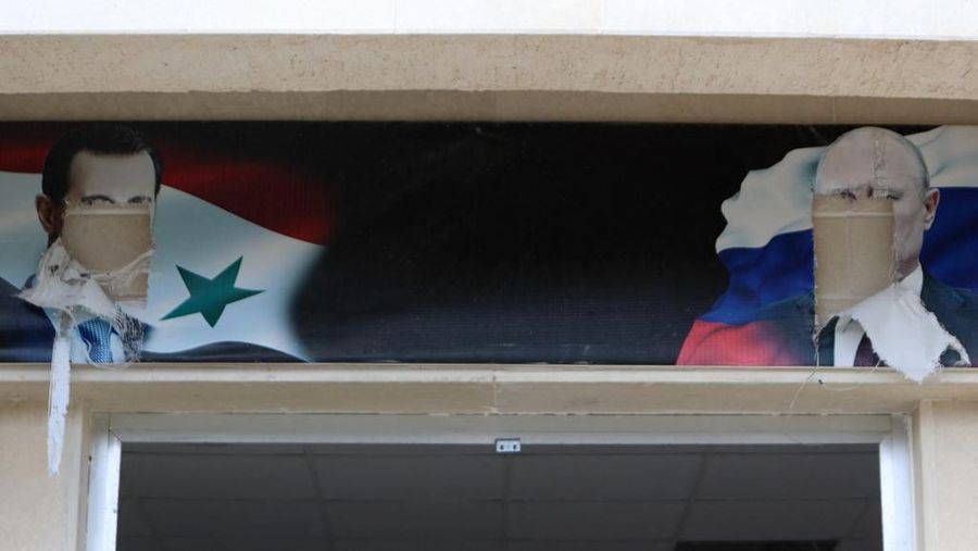 The defaced portraits of toppled Syrian president Bashar al-Assad and Russia's President Vladimir Putin hang above an entrance to a building, reportedly used by the Russian Army, in the in the Syrian town of Al-Bassah in the Latakia province on December 12, 2024. Islamist-led rebels took the Syrian capital Damascus in a lightning offensive on December 8, ousting president Bashar al-Assad and ending five decades of Baath rule in the country. (Photo by AAREF WATAD / AFP)