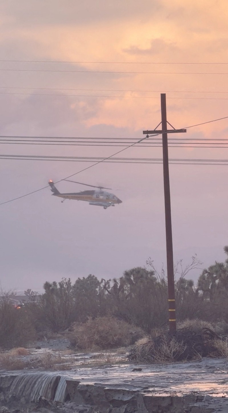 People sit on the roof of a building while they are stranded during floods partially submerging the surrounding area in the aftermath of torrential rains, in San Bernardino County, California, U.S. December 24, 2025 in this screengrab obtained from a social media video. Timothy and the Machine Music via Facebook/via REUTERS  THIS IMAGE HAS BEEN SUPPLIED BY A THIRD PARTY. MANDATORY CREDIT. NO RESALES. NO ARCHIVES.  Verification: Road layout, buildings and utility poles matched file and satellite images Date verified by original file metadata