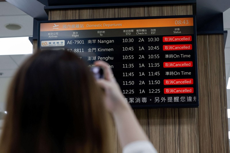 A person takes a photo of a flight information display screen that shows cancelled flights at the Taipei Songshan Airport, as China conducts